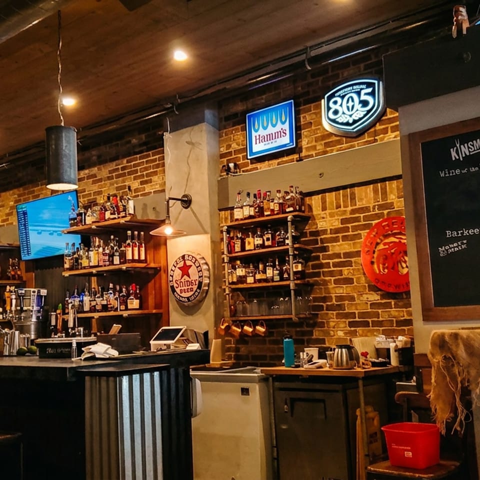Rustic bar interior with exposed brick, liquor shelves, televisions, draft taps, and a chalkboard menu.